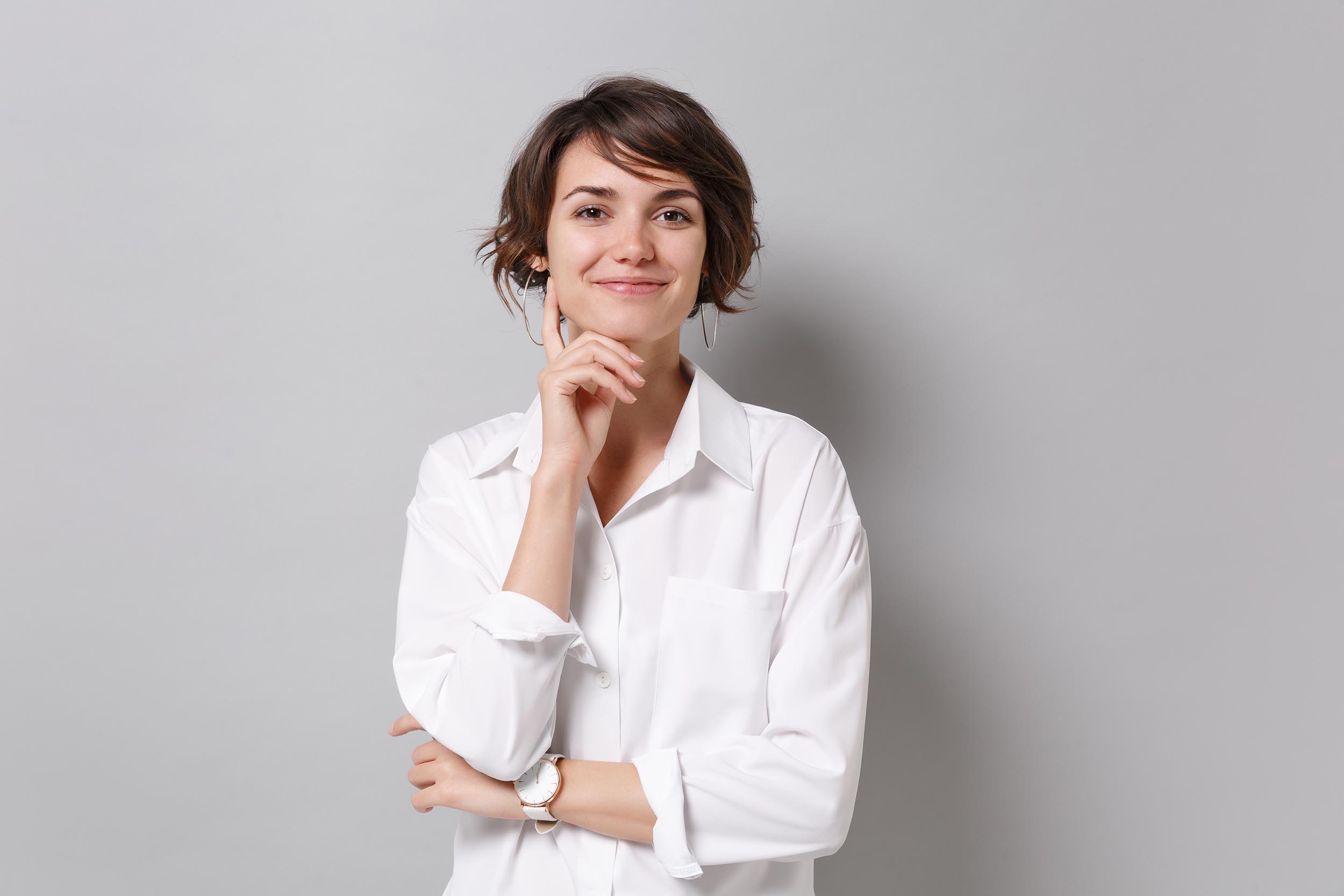 Smiling young business woman in white shirt posing isolated on grey background studio portrait. Achievement career wealth business concept. Mock up copy space. Put hand prop up on chin looking camera. emergency dentist in houston tx - adonia dentistry